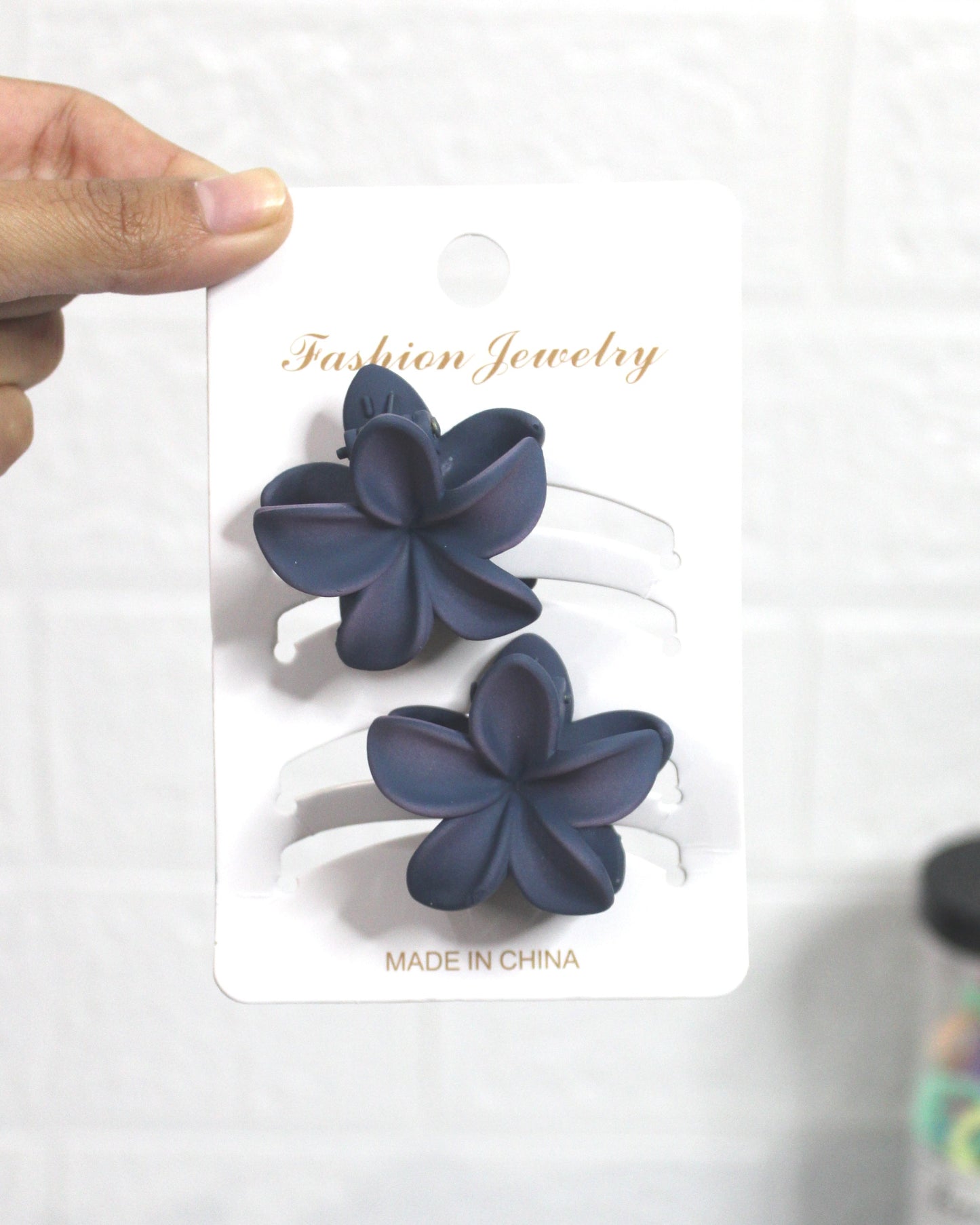 Navy blue flower-shaped hair accessories on a white card held by a hand, with colorful hair ties in the background.